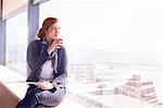 Pensive businesswoman with digital tablet drinking coffee at sunny urban window