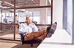 Pensive businessman sitting with feet up looking through sunny window in office