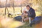 Young couple hikers resting in sunny grass using cell phone and digital tablet