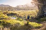 Young man with backpack hiking in sunny, remote field