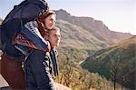 Affectionate young couple with backpack hiking, taking a break in sunny landscape