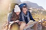 Young couple with backpacks hiking, resting and checking map and smart phone