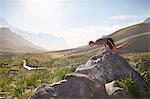 Young man balancing on hands on rock in sunny, remote valley