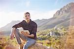 Young man using digital tablet on rock in sunny, remote valley