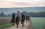 A string or group of riders on thoroughbred horses riding along a path. Racehorses in training. Routine exercise.