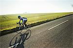 A cyclist riding along a country road on a clear sunny winter day. Shadow on the road surface.