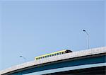 A yellow schoolbus driving over an elevated roadway against a blue sky.