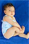 One year old baby girl wearing a swimsuit lying down on a blue beach towel