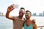 Two young men taking smartphone selfie on waterfront, New York, USA