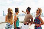 Four adult friends pointing at skyline from waterfront, New York, USA