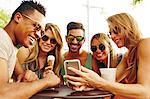 Five adult friends looking at smartphone at park table