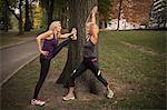 Two mature female friends training in park, stretching