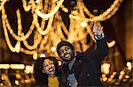Couple taking smartphone selfie by Christmas lights at night, New York, USA