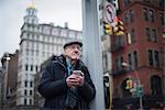 Man leaning against lamppost holding smartphone, Manhattan, New York, USA