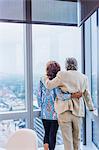 Senior couple looking out of window of tall building, rear view