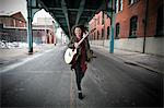 Young woman running below elevated road with acoustic guitar