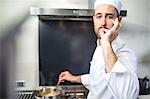 Portrait of chef stirring pan on stove, signalling with fingers to lips