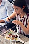 Woman using smarphone to photograph her meal in restaurant