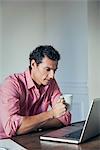 Man drinking coffee while using laptop computer