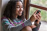 Portrait of beautiful happy mixed race African American girl teenager female young woman smiling with perfect teeth using mobile cell phone for social media or texting,