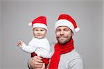 Father with his baby boy wearing Santa hats celebrating Christmas