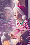 happy smiling boy holding nicely wrapped gift sitting cozy at home looking out the window while snowing waiting for christmas miracle, christmas lights and decorations, holiday concept, toned image