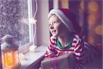 happy smiling boy holding nicely wrapped gift sitting cozy at home looking out the window while snowing waiting for christmas miracle, christmas lights and decorations, holiday concept, toned image