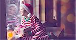 panorama of happy smiling boy holding nicely wrapped gift sitting cozy at home looking out the window while snowing waiting for christmas miracle, christmas lights and decorations, holiday concept, toned image