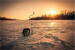 Ice fishing scene with box, drill and a rod on river during sunset