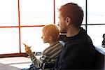 family of two, father and son, waiting together at the airport for plane departure, kid holding toy plane, sun flare, vacation and travel concept