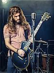 Photo of a young man with long hair and beard playing electric guitar on stage.