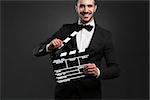 Portrait of a beautiful latin man with tuxedo and holding a clapboard