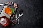 Tea cup, teapot and assortment of dry tea in spoons on stone table. Top view with copy space