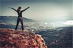 Cheering young woman standing at sunrise seaside mountain peak. Arms outstretched, freedom and happiness, achievement in mountains. Back view