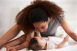 Mother Playing With Baby Daughter In Bedroom At Home