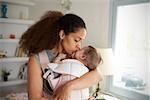 Mother Cuddling Baby Daughter At Home In Front Of Window