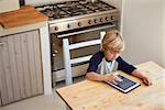 Young boy using tablet computer in kitchen, elevated view