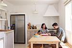 Two teenagers using laptop study together at kitchen table