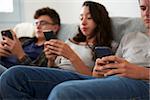 Three teenagers sitting together using smartphones at home