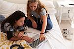 Two teenage girls on bed using laptop, elevated view close up