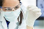 Female medical or research scientist or doctor using looking at a test tube of clear solution in a lab or laboratory