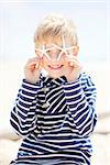 adorable smiling little boy in striped sweater holding two starfish and being playful at the beach, vacation concept