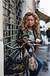 Woman with bicycle in street looking at smartphone