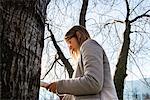 Young woman standing beside tree, reading book, low angle view