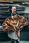 Portrait of male metalworker holding copper product, forge storeroom