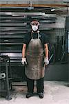 Portrait of male metalworker in dust mask, forge storeroom