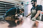 Two metalworkers cutting sheet copper at forge workbench