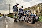 Senior male motorcyclist talking to grandson sitting on motorcycle on rural roadside