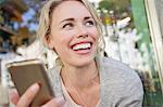 Mid adult woman holding smartphone at city sidewalk cafe