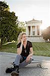 Female skateboarder sitting on skateboard in park making smartphone call